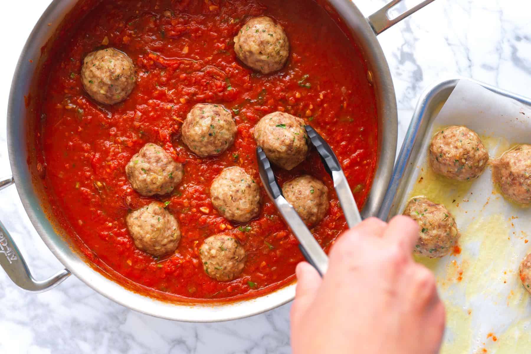 Putting baked meatballs into homemade marinara sauce ready for spaghetti and meatballs