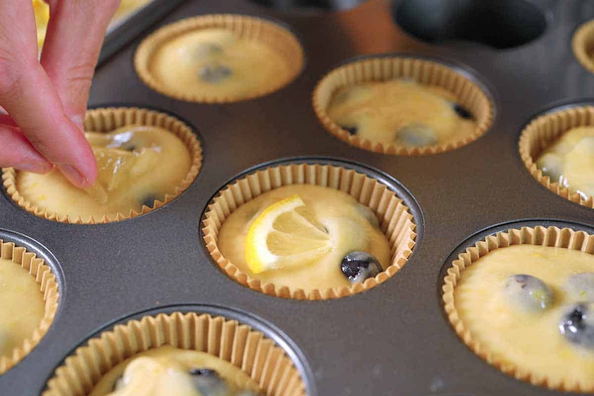 Adding a slice of lemon to lemon blueberry muffins in muffin tin