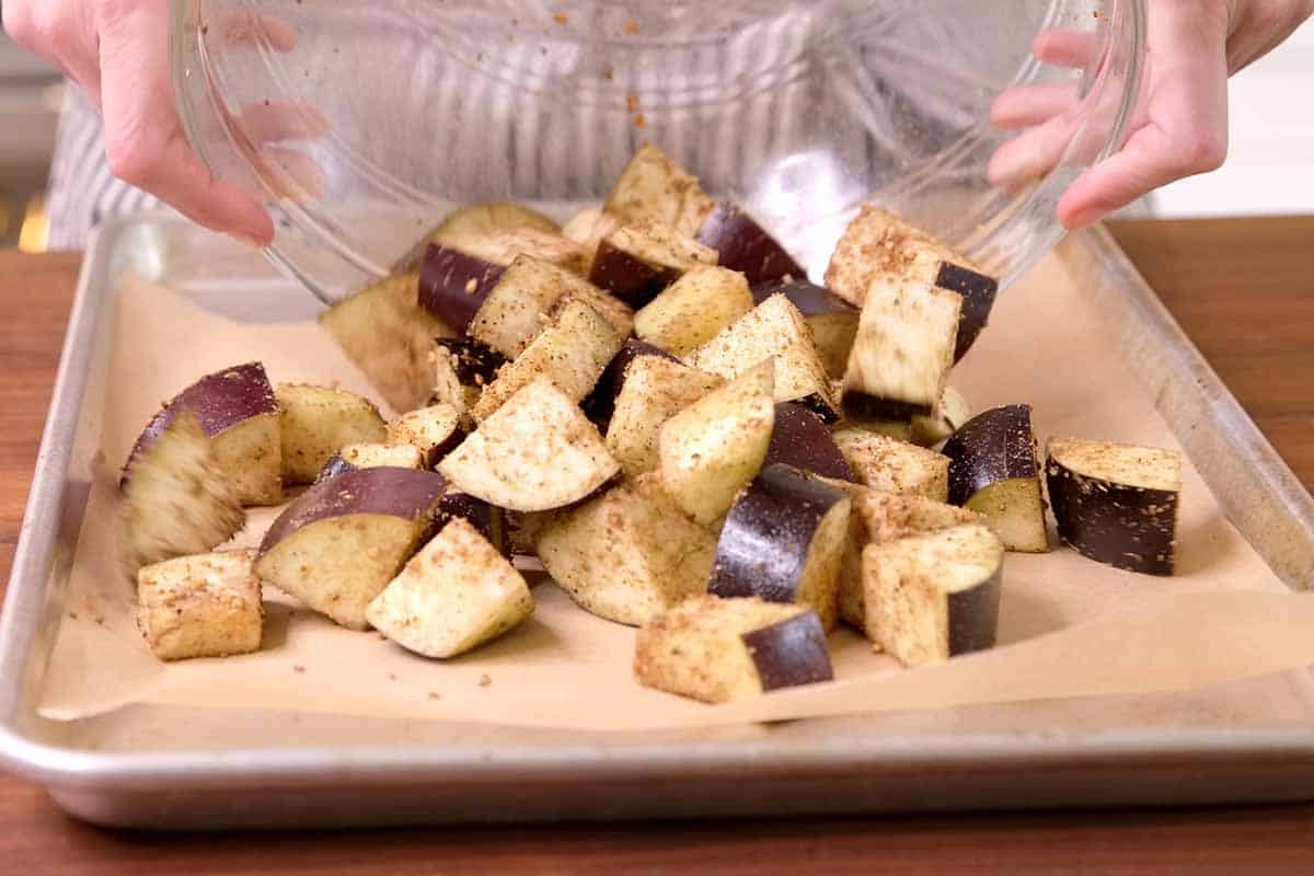 Adding eggplant to a baking sheet before roasting it in the oven