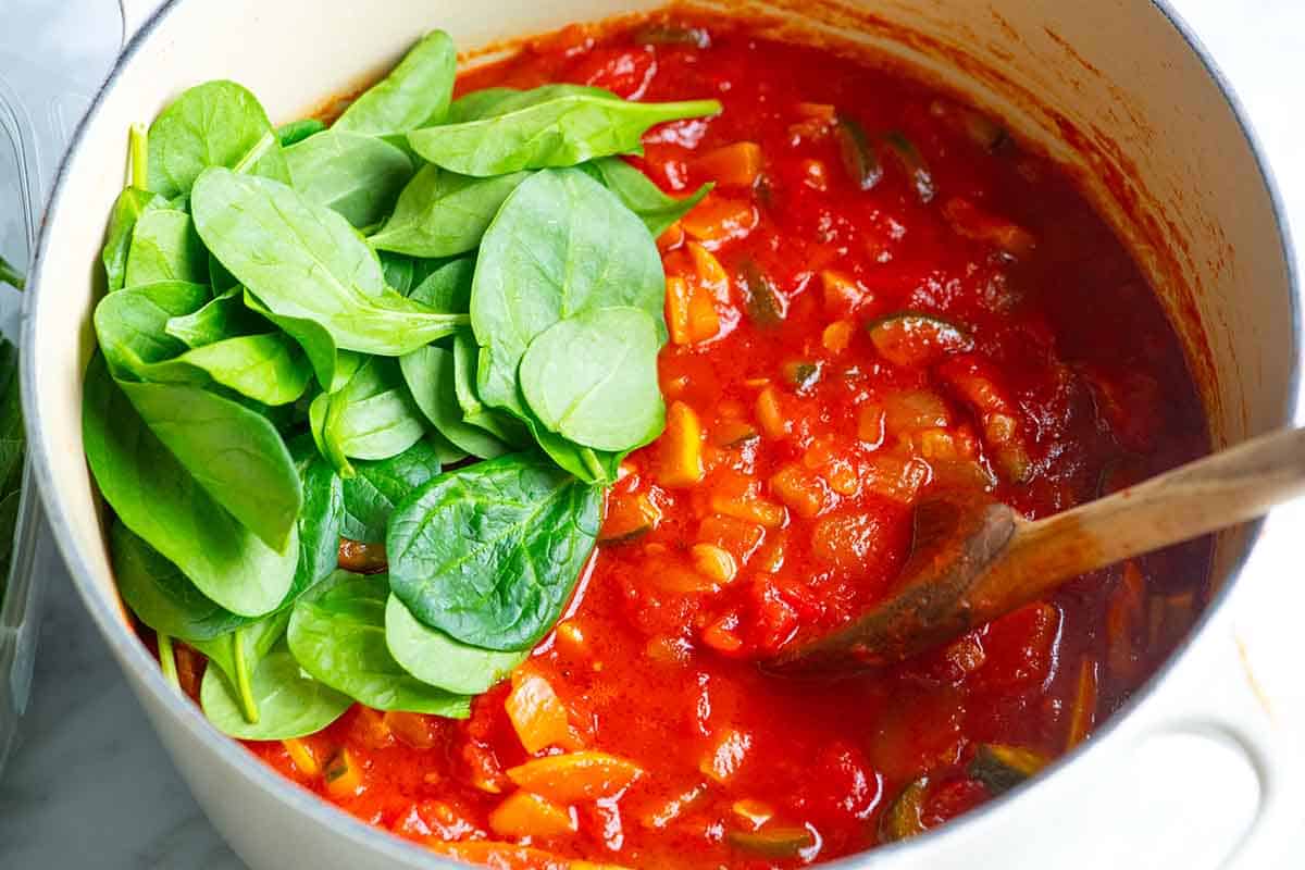 Making the vegetable sauce for the pasta. Stirring in fresh spinach and basil.