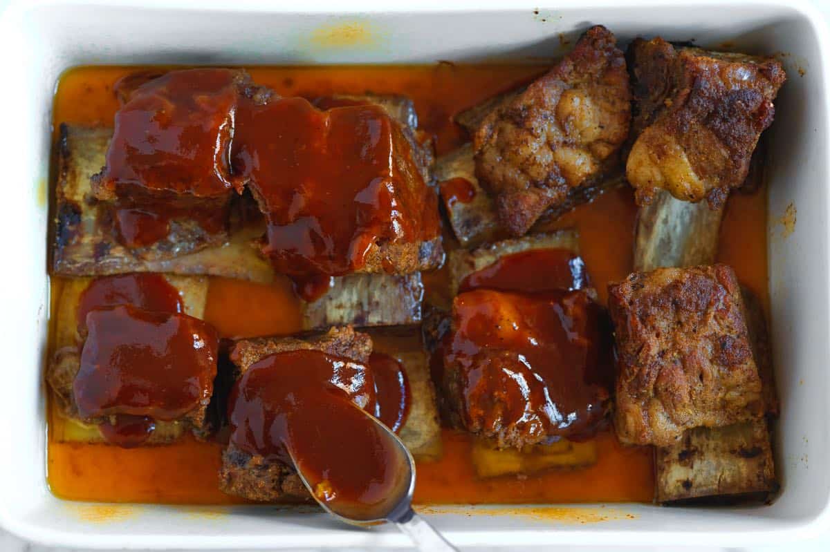 Spooning BBQ sauce over tender baked beef ribs