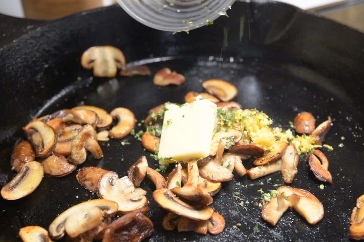 Seasoning cooked mushrooms with lemon, garlic, salt, and pepper.