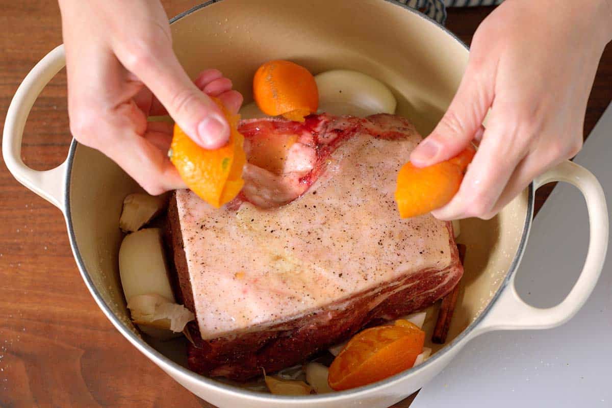 Seasoned pork shoulder with oranges, onions, garlic, and a cinnamon stick in a Dutch oven