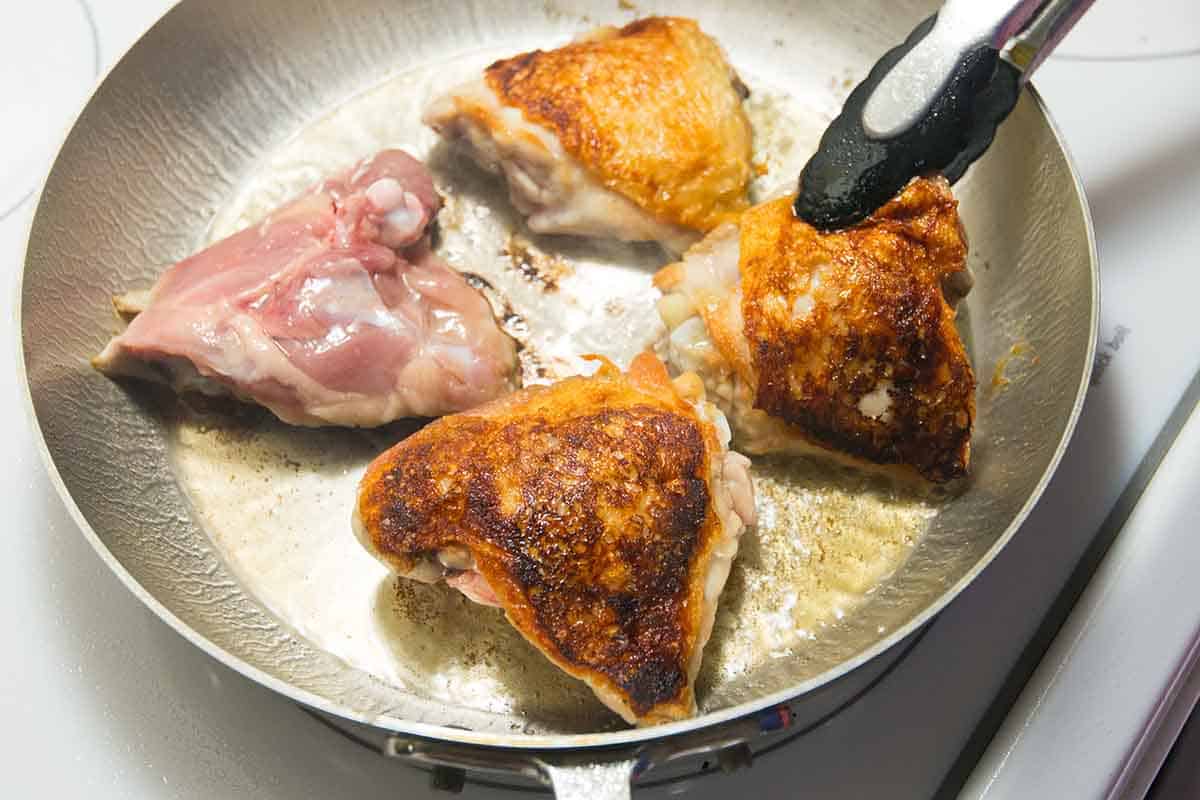 Browning skin-on chicken thighs in a skillet