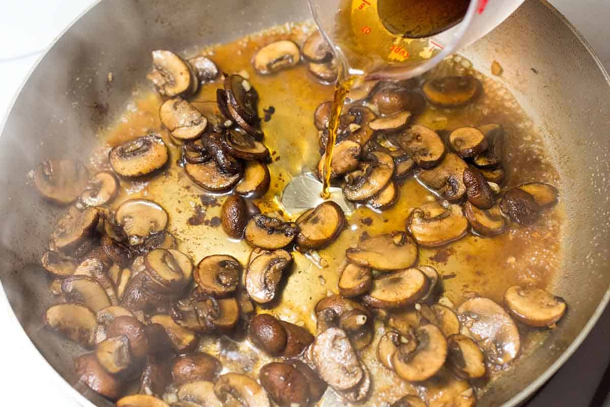 Pouring Marsala wine into mushrooms in a skillet