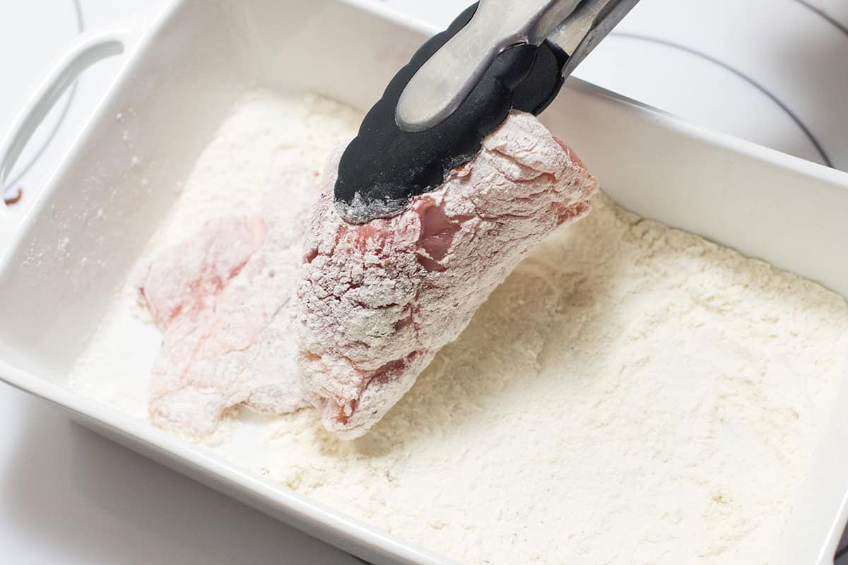 Dredging chicken in flour before cooking in a skillet