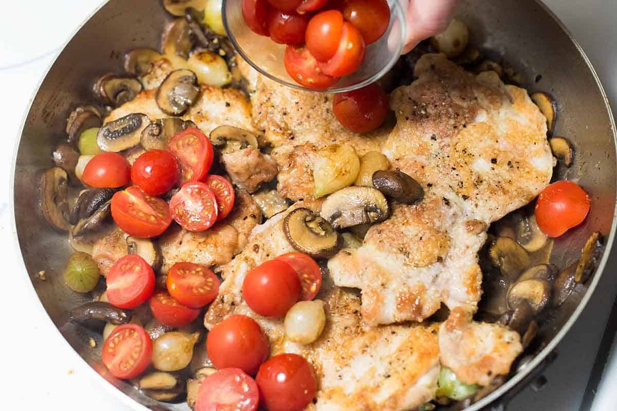 Adding optional cherry tomatoes to the skillet with chicken, mushrooms, and Marsala sauce