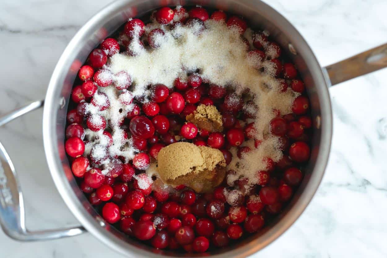 Cranberries in a saucepan with orange juice, lemon juice, and sugar for homemade cranberry sauce