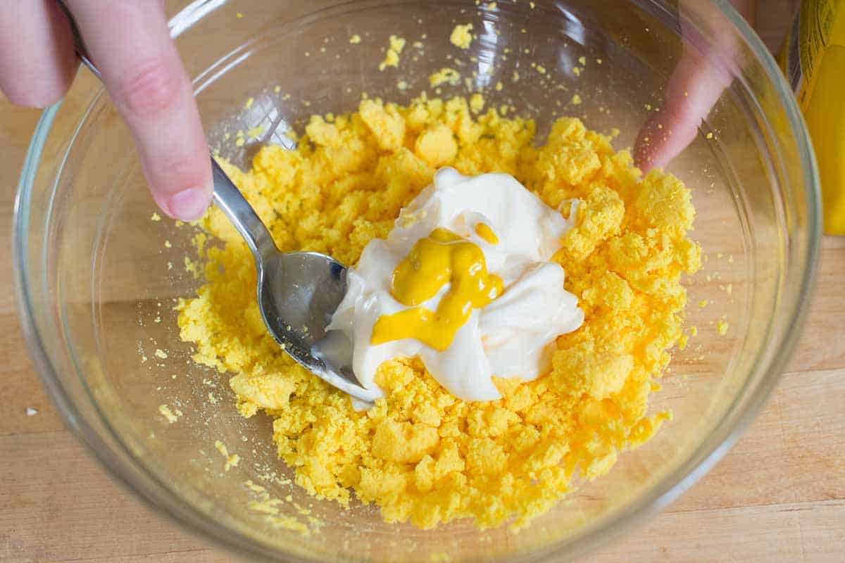 Stirring mayonnaise and mustard into egg yolks for deviled eggs filling