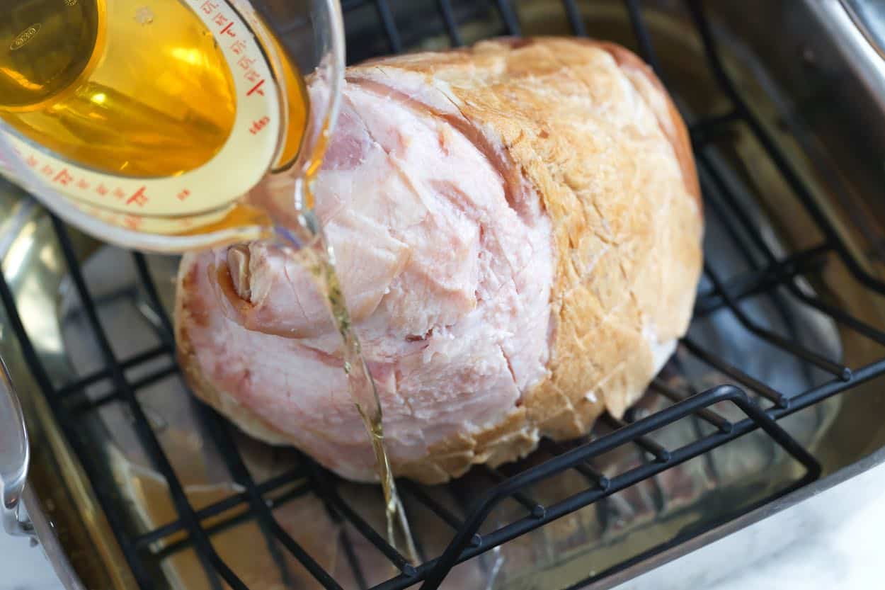 Adding apple juice to a roasting pan with ham ready to bake in the oven