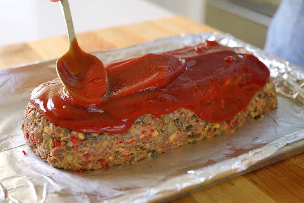 Spreading glaze over unbaked meatloaf on a sheet pan
