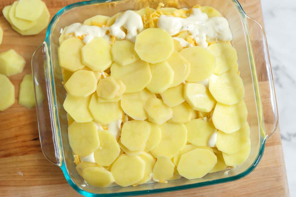 Layering sliced potatoes with cheese and au gratin sauce in a baking dish