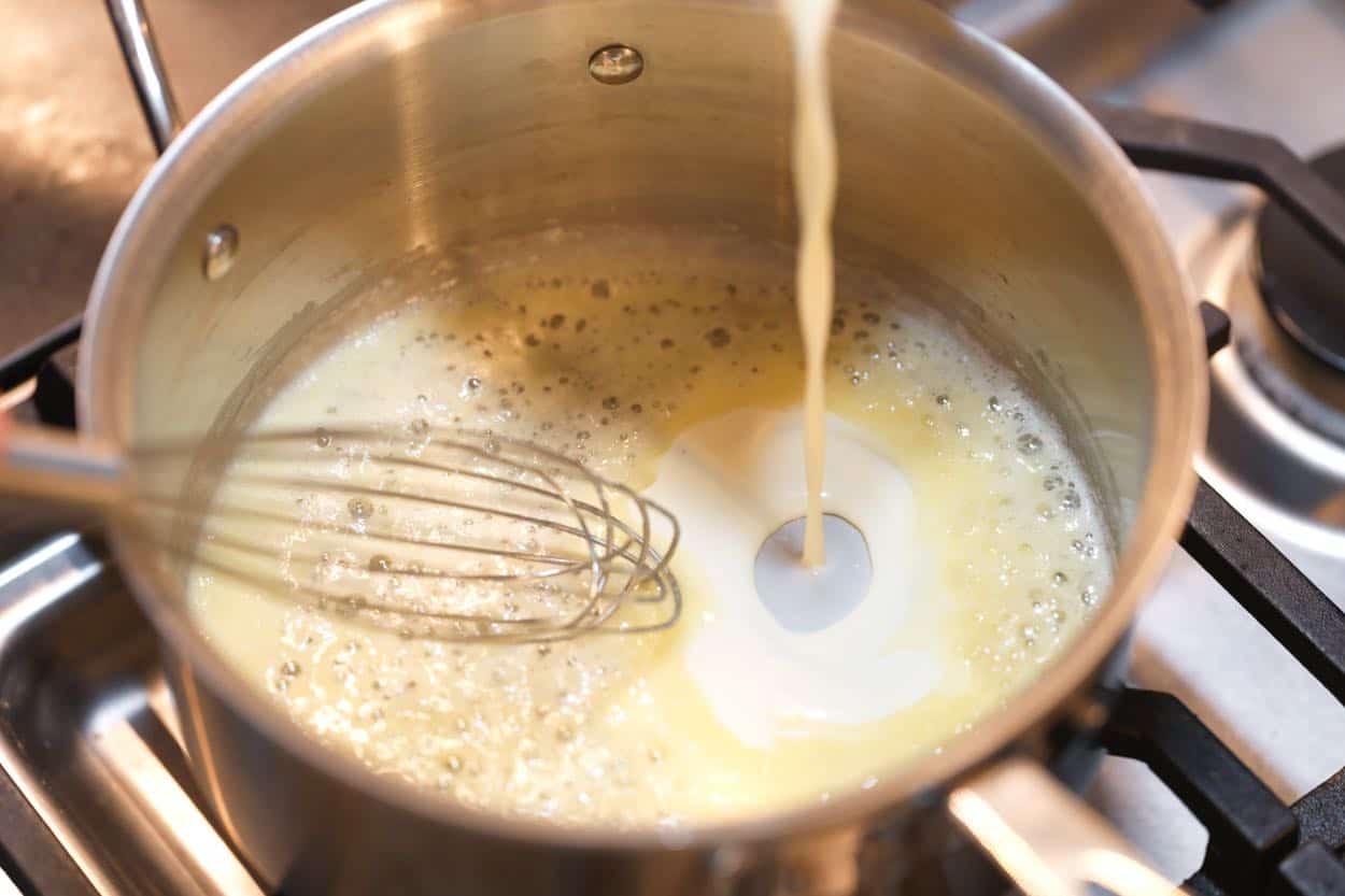 Whisking milk and cream into a roux made with butter and flour