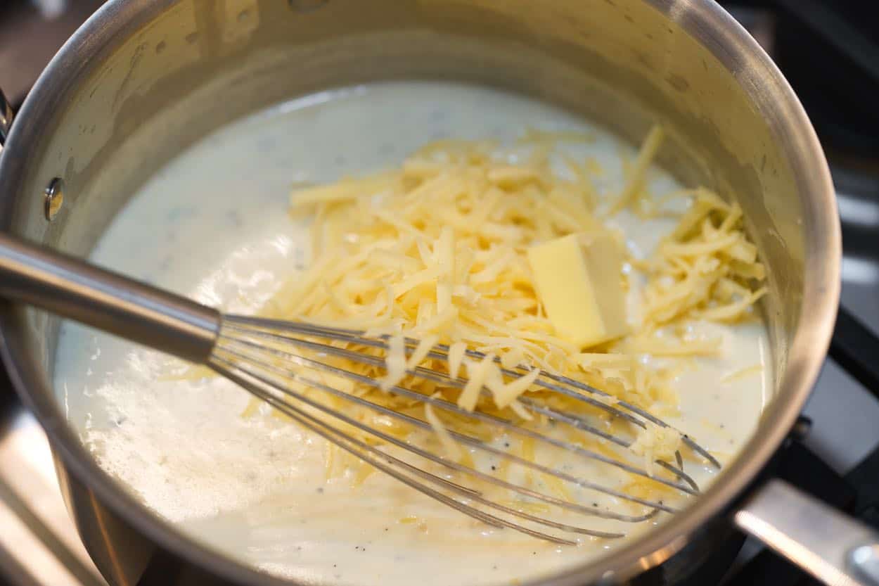 Whisking grated Gruyere cheese and butter into the sauce for scalloped potatoes