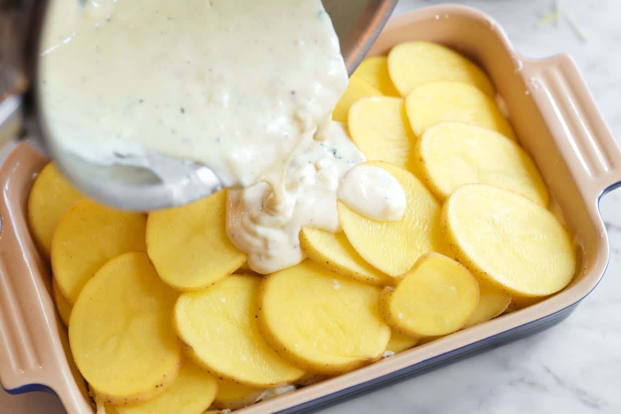 Layering cream sauce and potato slices in a baking dish