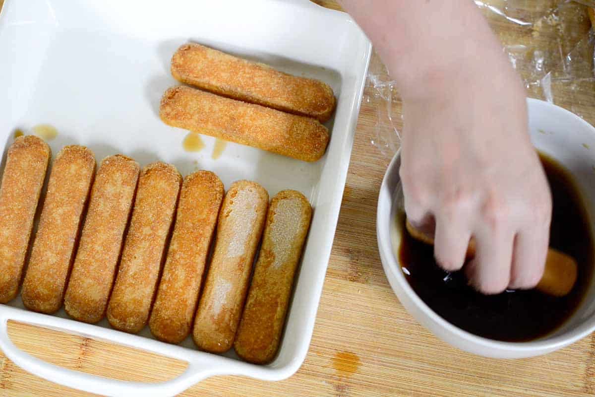 Dipping ladyfingers into coffee mixture for assembling tiramisu