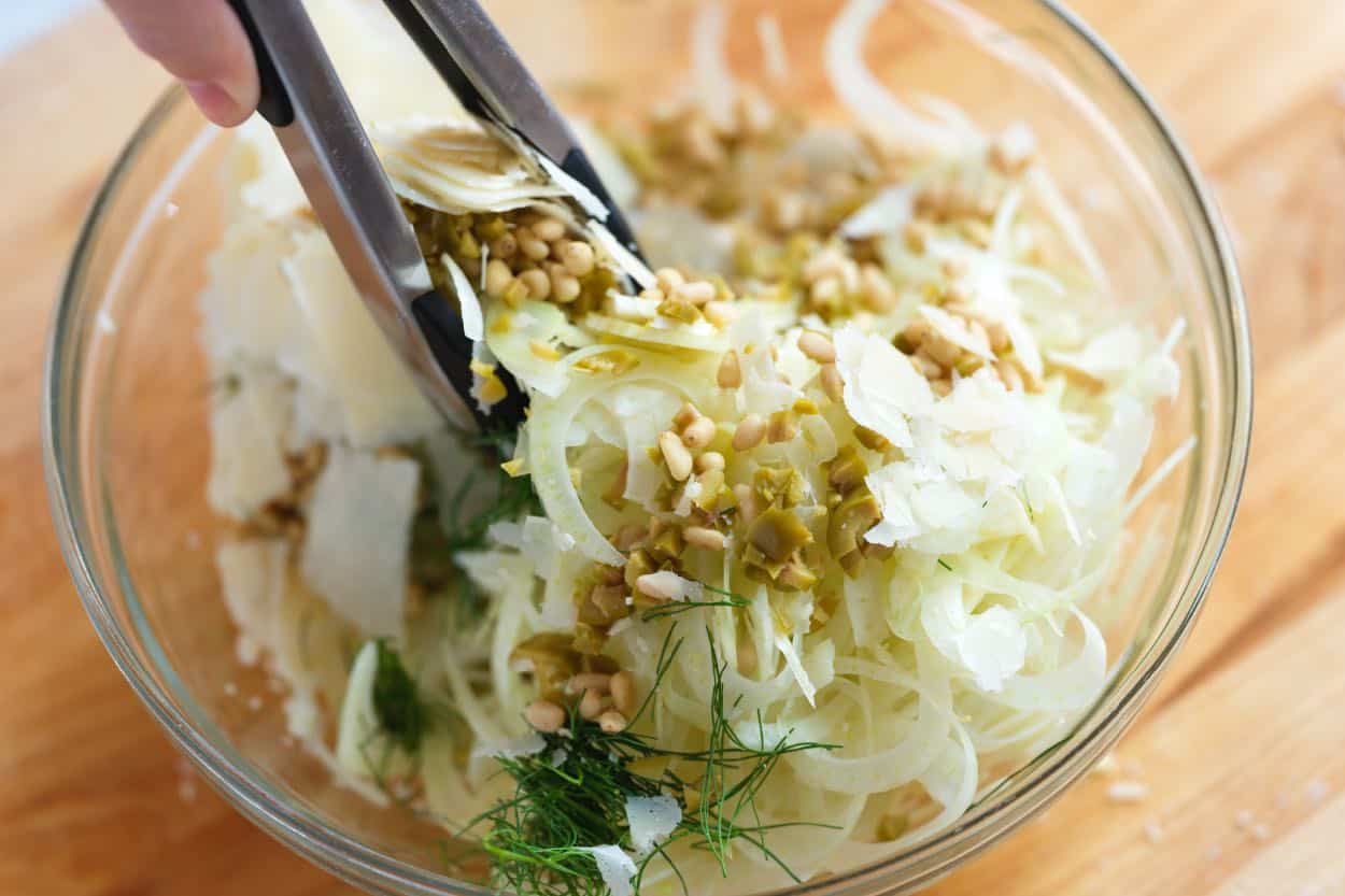 Tossing the fennel, nuts, olives, and cheese with the lemon dressing.