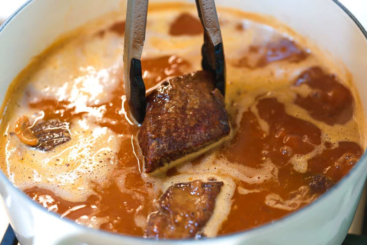 Placing browned beef short ribs into braising liquid