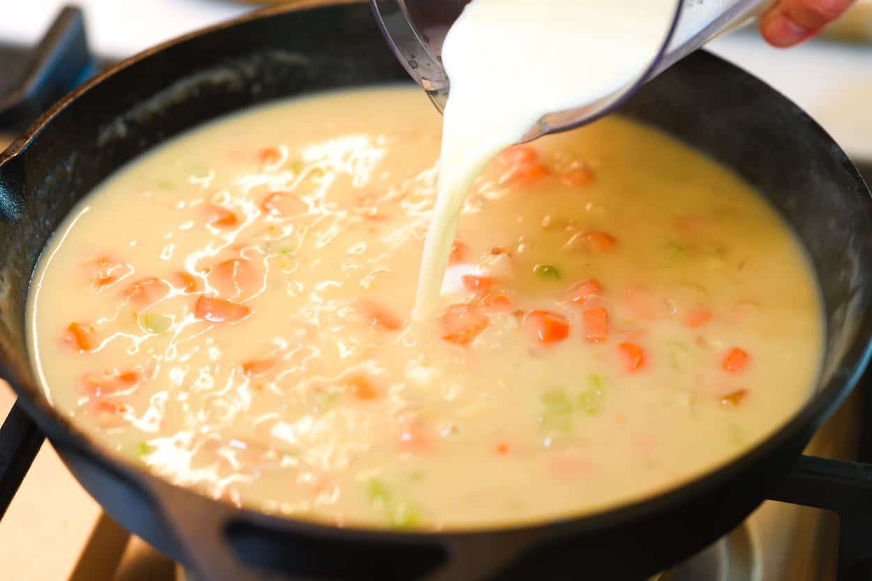 Pouring milk into the gravy to make the pot pie filling creamy