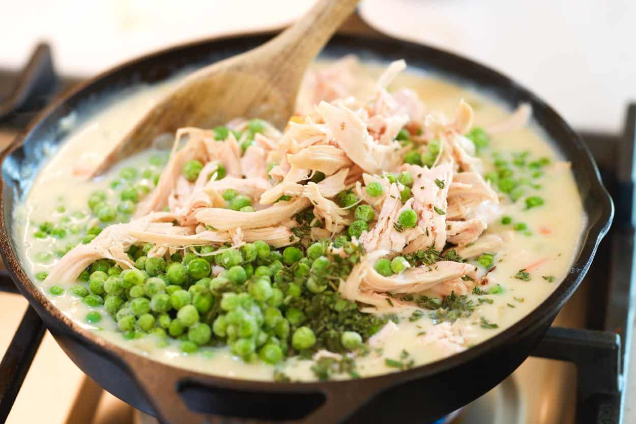 Folding shredded rotisserie chicken and peas into the pot pie filling.