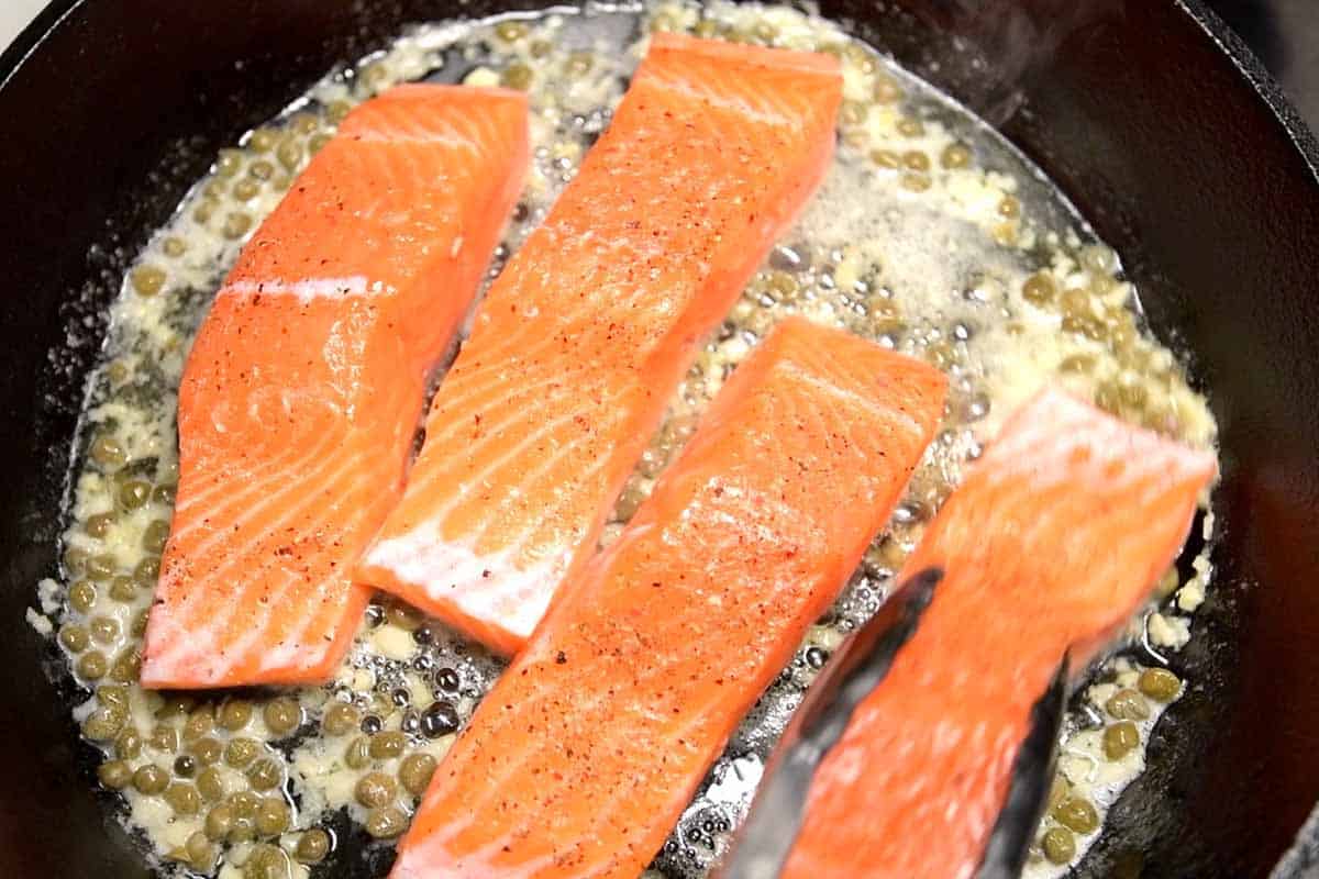 Seasoned salmon fillets in an oven-safe skillet in the caper butter ready to bake.