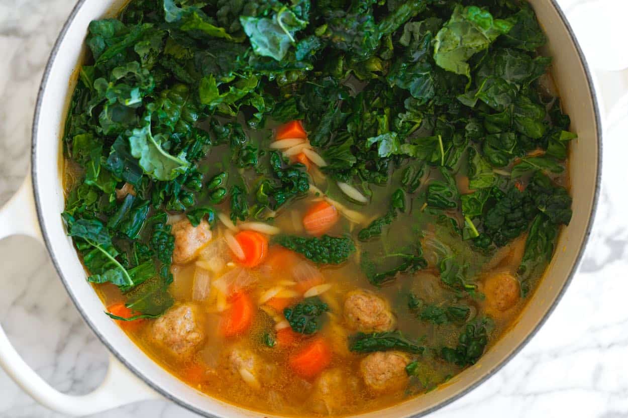 Stirring kale into turkey meatball soup with orzo
