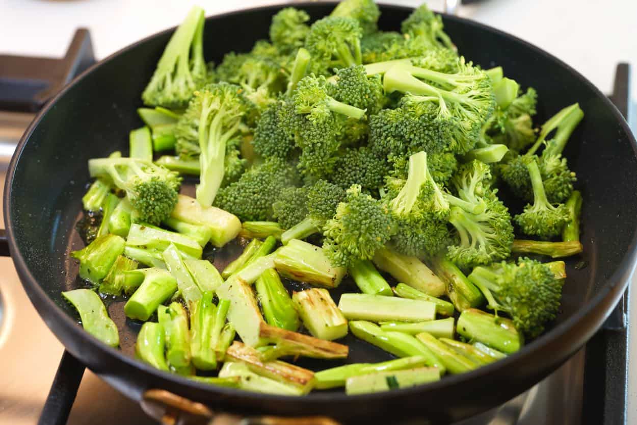 Adding broccoli florets to the skillet with browned broccoli stems.