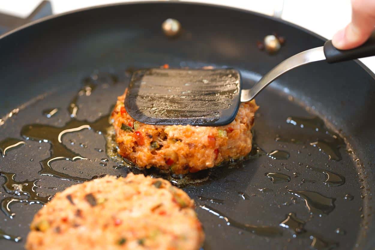 Cooking chicken burgers in a skillet to brown on both sides.