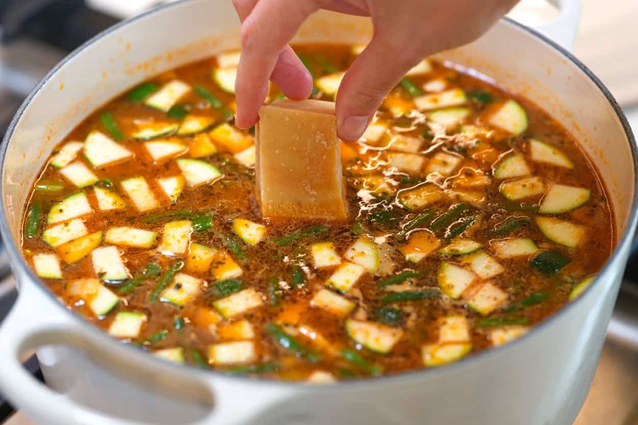 Dropping Parmigiano-Reggiano rind into the minestrone to simmer.