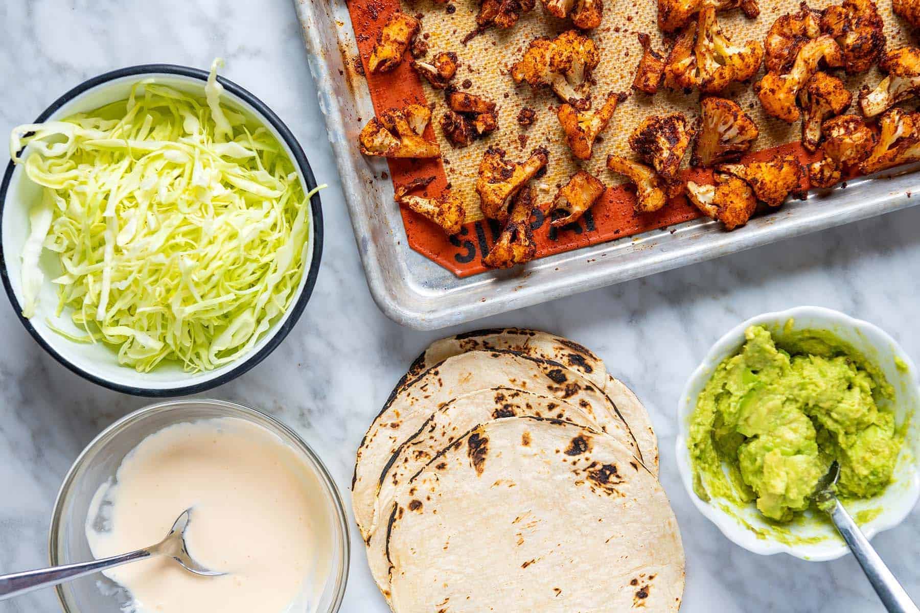 Building cauliflower tacos with roasted cauliflower, cabbage, lime sour cream, and mashed avocado