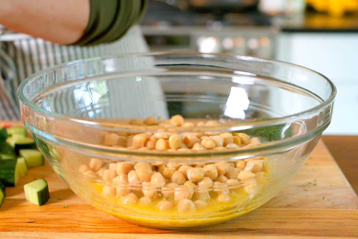 Making chickpea salad by adding chickpeas to the dressing in a big bowl