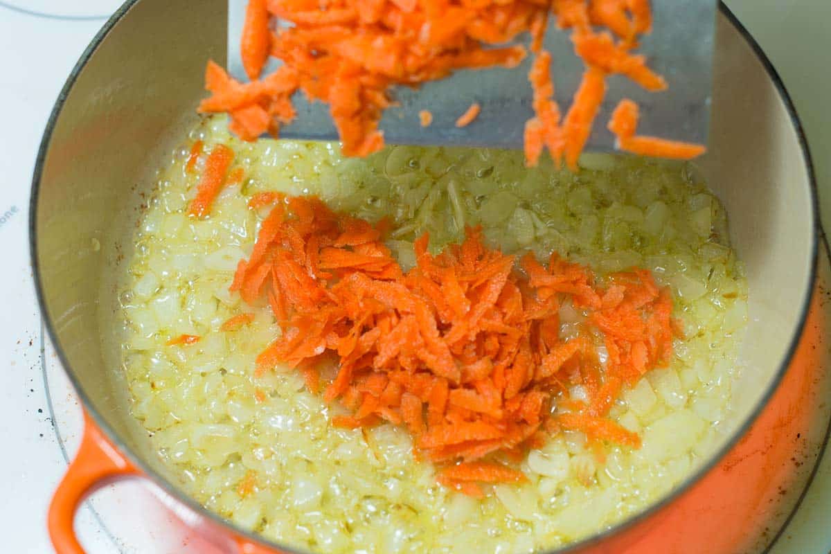 Adding grated carrots to the soft onions and garlic