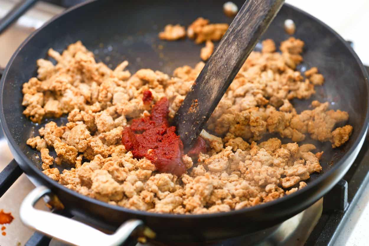 Stirring tomato paste into browned turkey meat for tacos