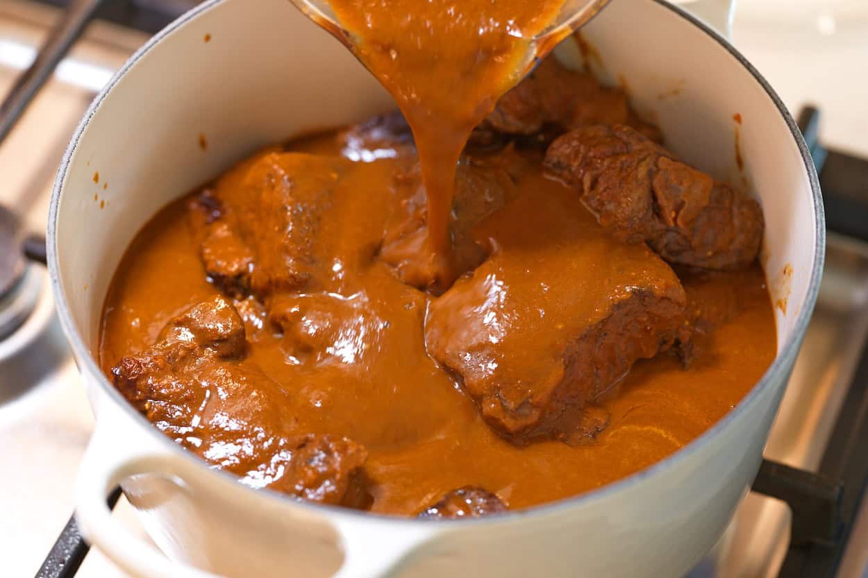 Pouring blended dried chilies, onion, spices, and broth over browned beef for birria