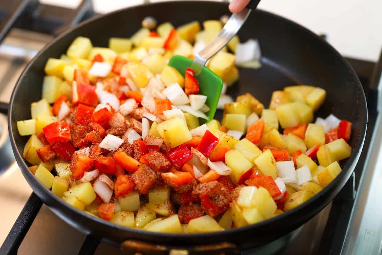Stirring the spice mix, bell pepper, and onion into the potatoes in the skillet