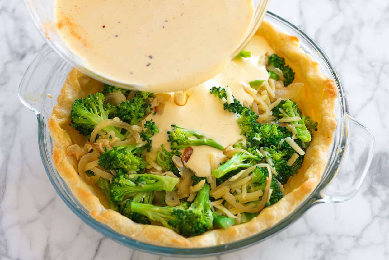 Pouring egg custard over broccoli, onion, and cheddar cheese for quiche