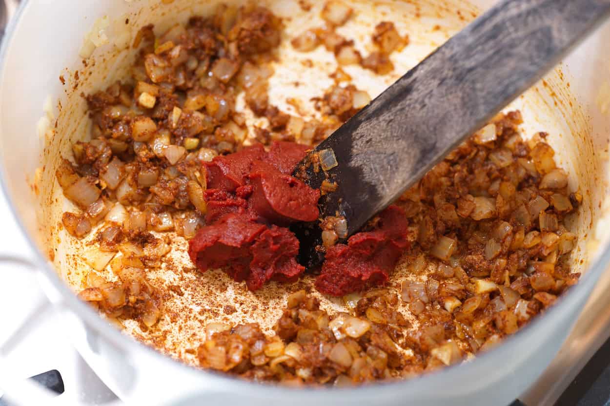 Stirring tomato paste into the pot with spices and onions for the tikka masala sauce