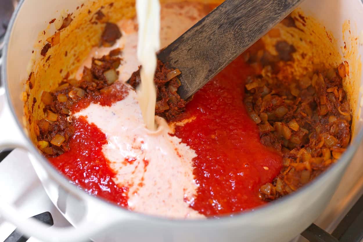 Pouring crushed tomatoes, broth, and cream to make the curry sauce