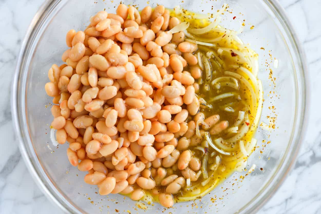A bowl with Italian dressing, onion, and white beans (the base for antipasto salad)