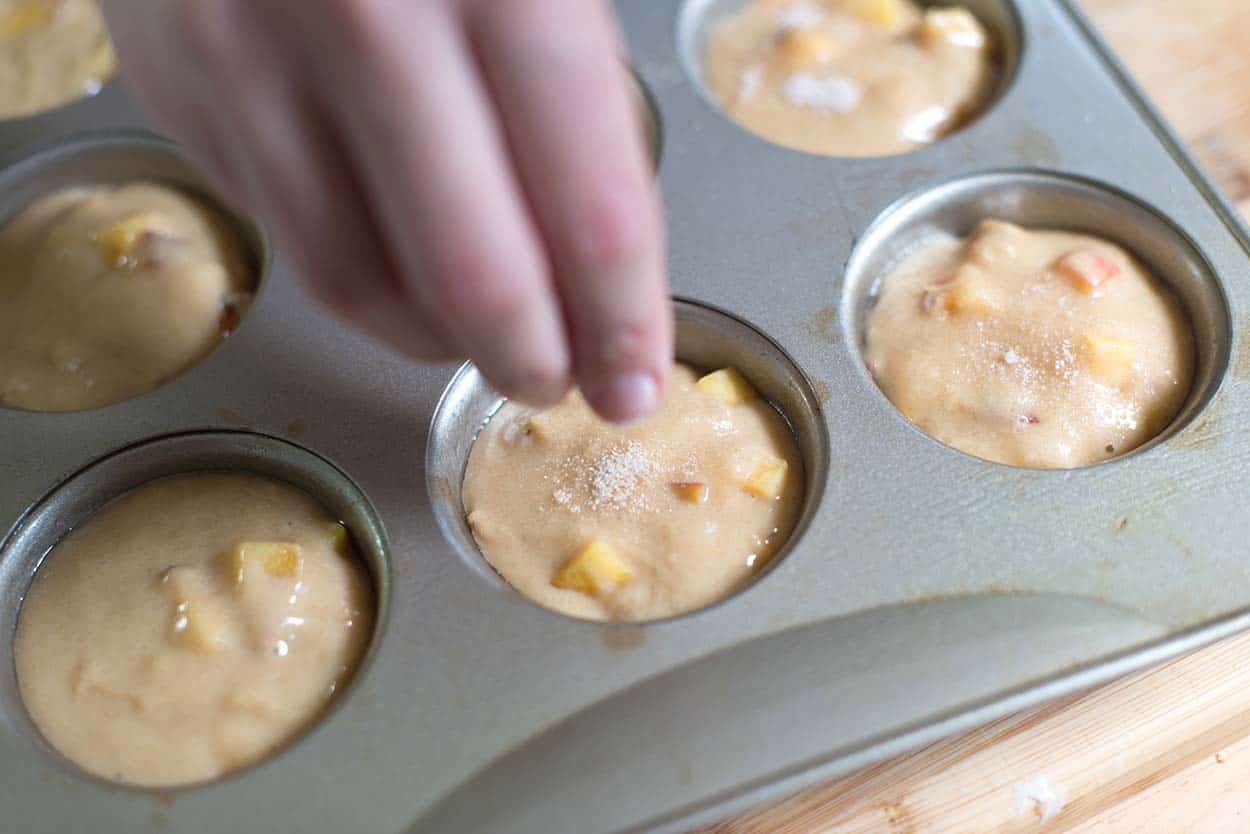 Sprinkling spiced sugar on the tops of the peach muffin batter before baking