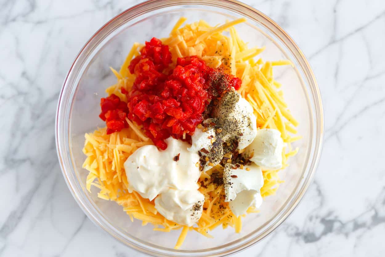 Pimento cheese ingredients in a bowl (cheddar, cream cheese, mayo, pimento peppers, and spices)
