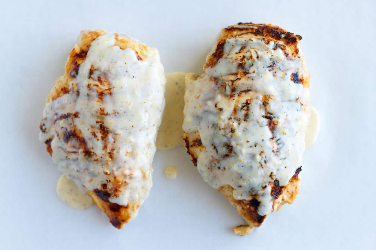 Pouring leftover marinade over the grilled chicken before baking in the oven