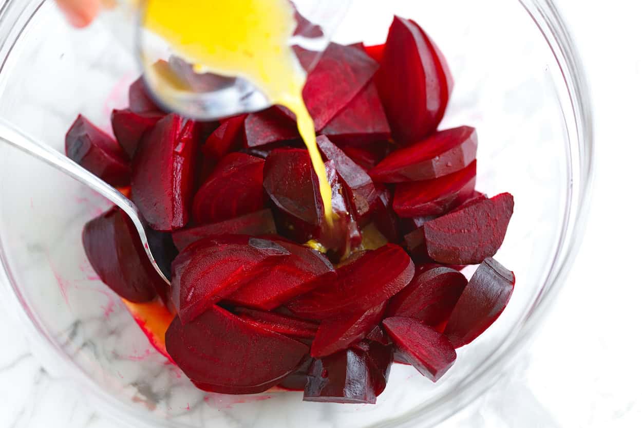 Pouring the dressing over roasted beets in a bowl