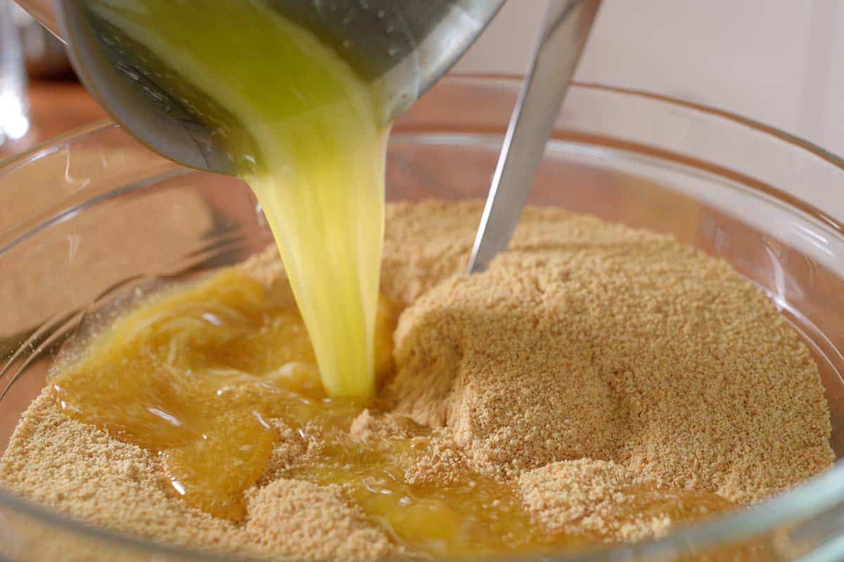 Pouring butter into graham cracker crumbs and sugar for a cheesecake crust