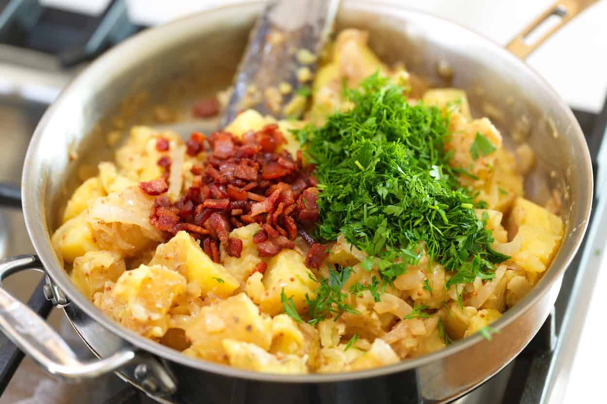 Adding crispy bacon, fresh dill, and fresh parsley to potatoes in a skillet