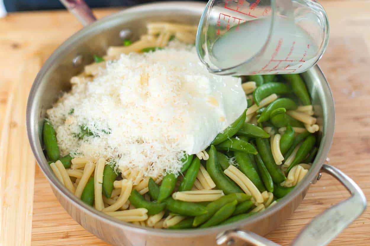 Pouring hot pasta cooking water into the pan to thin the sauce.