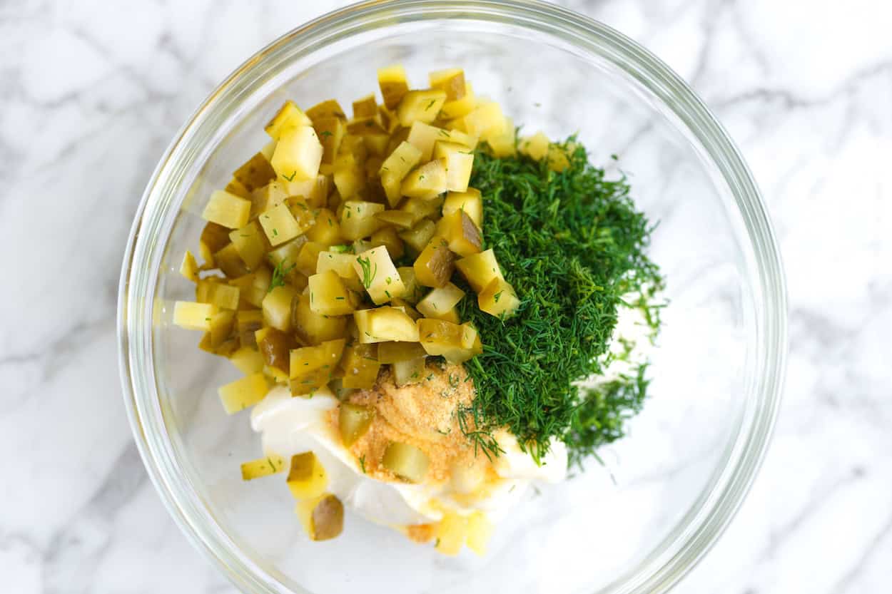 Making pickle dip in a bowl with sour cream, pickles, and fresh dill
