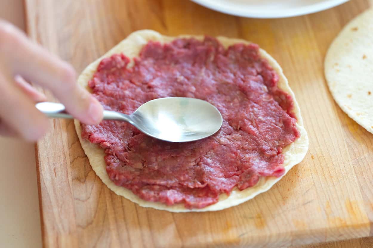 Spreading ground beef on a flour tortilla for smash burger tacos
