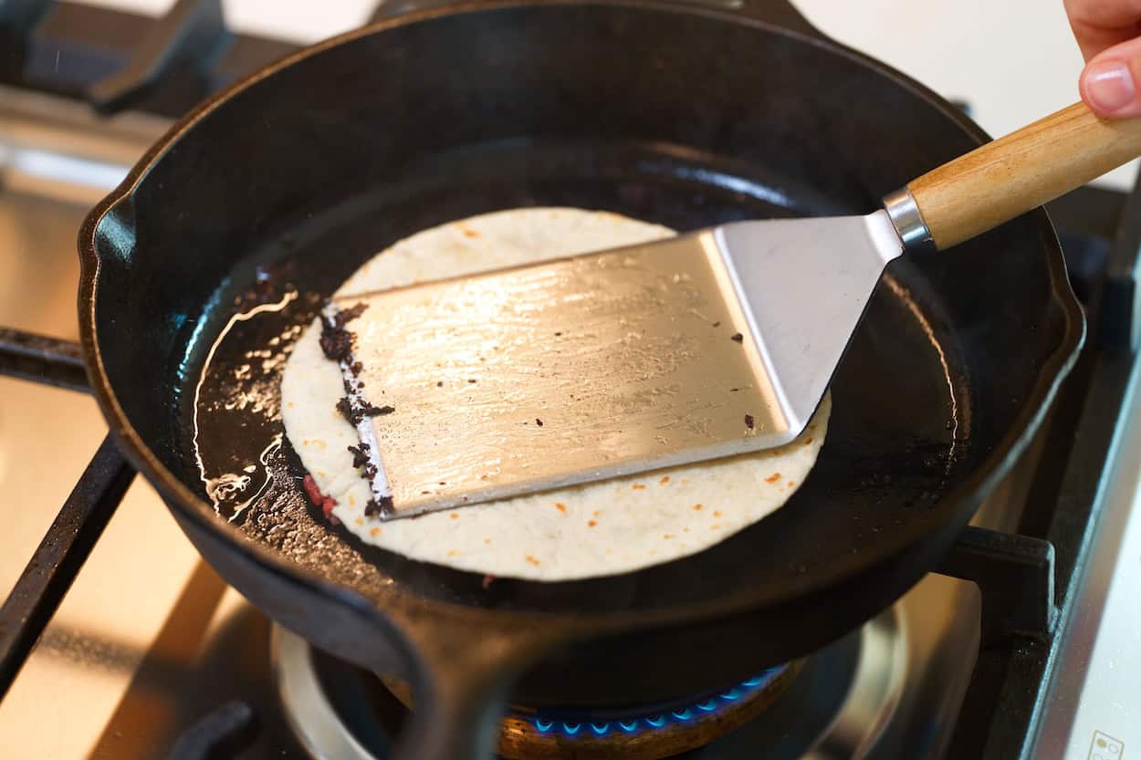 Pressing a smash burger taco in a pan