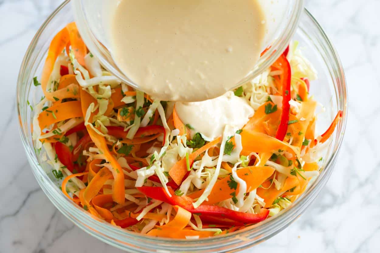 Pouring the Asian slaw dressing over the slaw ingredients